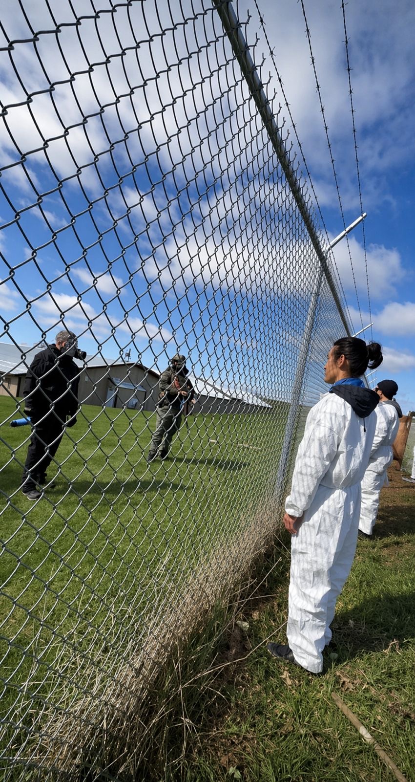 An activist observes police beyond the fence.