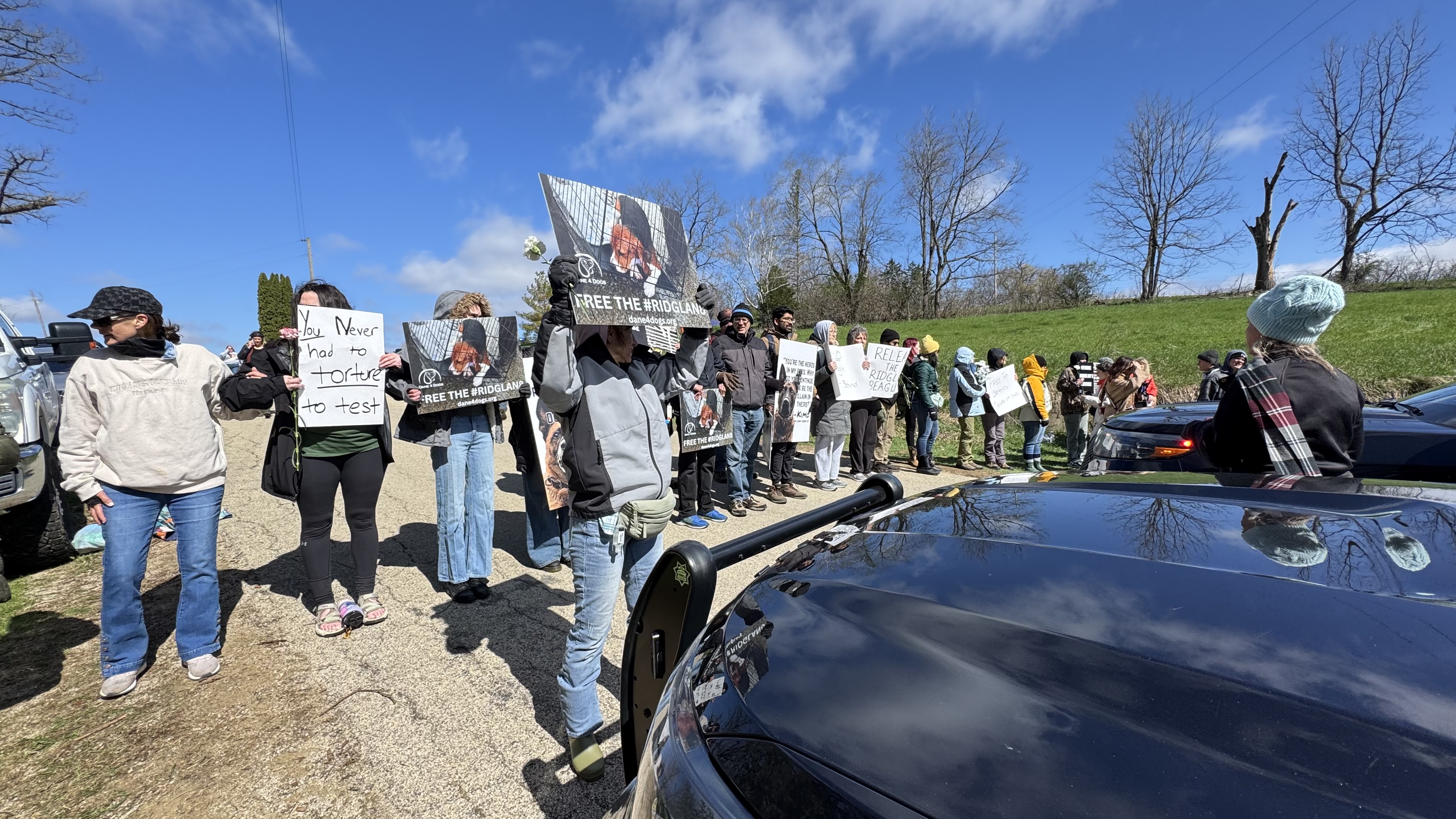 Activists hold signs in front of a police vehicle.